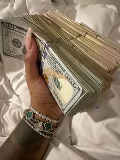 a person holding stacks of money on top of a bed