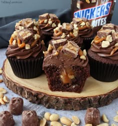 chocolate cupcakes with peanut butter frosting and nuts on a wooden board next to a jar of snickkers bites