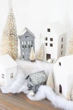 some white houses and trees on a wooden floor with snow around them, as well as christmas decorations