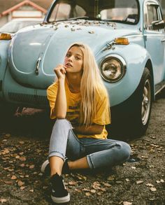 a woman sitting on the ground next to a blue vw bug car in front of her