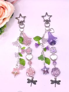 two pairs of earrings with charms hanging from them on a white table next to flowers