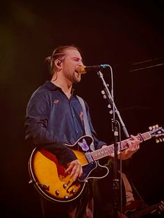 a man standing in front of a microphone while holding a guitar and singing into a microphone