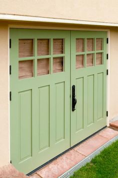 a green garage door with two windows on the side and grass in front of it