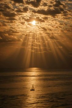 the sun shining through clouds over water with a sailboat in the foreground and another boat on the far side