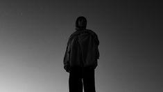 a man standing on top of a snowboard under a gray sky with the sun behind him