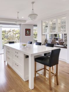 a large kitchen with white counter tops and black leather bar stools next to an island