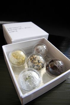 four different types of donuts in a white box on a black counter top with the lid open