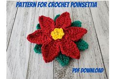 a crocheted poinsettia with a yellow center sits on a wooden surface