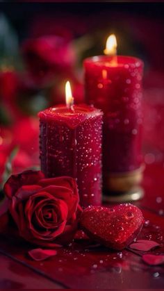 two red candles with hearts and roses on the table next to them, one is lit