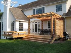 a large white house with a wooden deck and pergolated area in the front yard