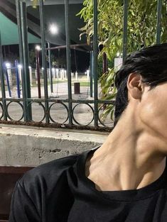 a woman sitting on a bench in front of a fence at night with her eyes closed