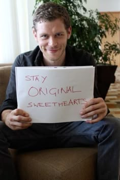 a man sitting in a chair holding a sign that says stay original, sweet hearts