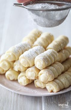 powdered sugar being poured onto pastries on a plate