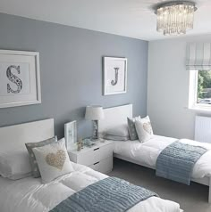 two beds in a room with blue walls and white bedding, one has a chandelier above the headboard