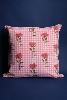 a pink and white gingham pillow with red flowers on the front, against a blue background