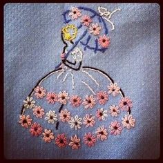 a embroidered picture of a woman in a blue dress with pink and white daisies