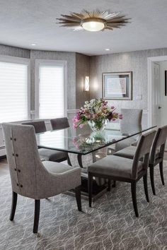 a dining room table with chairs and a vase on top of it in front of windows