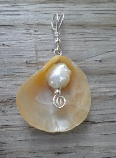 a large shell with a pearl in the center on a silver chain hanging from a wooden surface