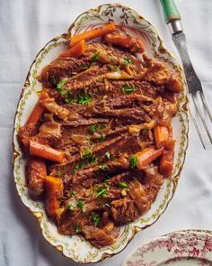 a plate with meat and carrots on it next to a fork, knife and spoon