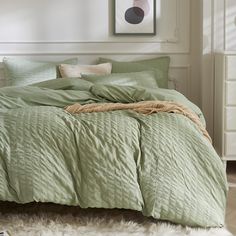 a bed with green comforter and pillows in a room next to a white dresser