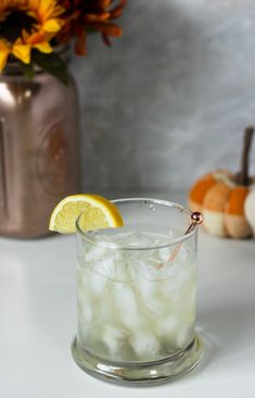 a glass filled with ice and lemon sitting on top of a table next to a vase