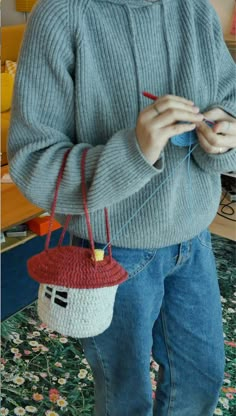 a woman holding a small knitted house with a red roof on it's side