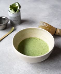 a white bowl filled with green liquid next to a brush