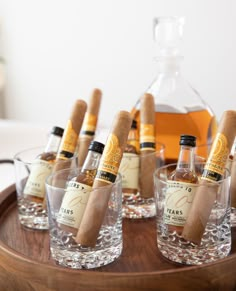 several bottles and glasses with cigars in them on a wooden tray next to a bottle