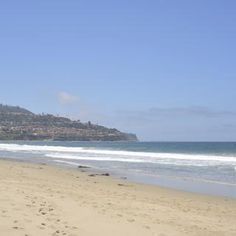 two people walking on the beach with their surfboards in hand and an ocean view behind them