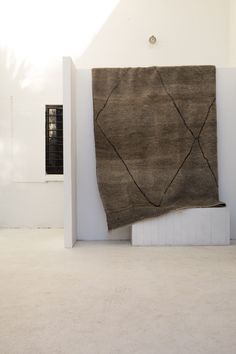 a large brown rug sitting on top of a floor next to a white wall and window