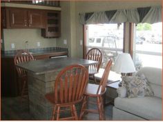 a kitchen and living room area in a mobile home with wood cabinets, granite counter tops, and wooden chairs