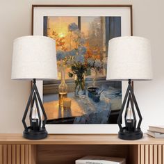 two lamps sitting on top of a wooden table next to a vase filled with flowers