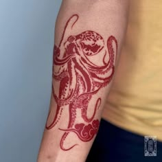 an octopus tattoo on the arm of a man's left arm, with red ink