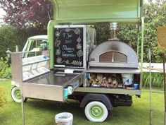 an outdoor food cart with a chalkboard sign on the back and wood stacked inside