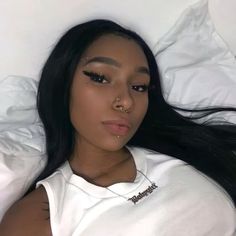 a woman laying on top of a bed wearing a white t - shirt and silver necklace