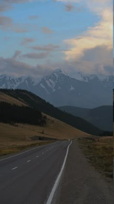 an empty road in the middle of nowhere with mountains in the background and snow on the tops