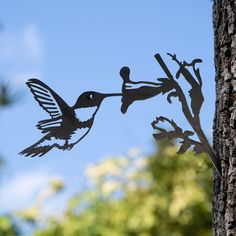 a metal bird sculpture hanging from the side of a tree