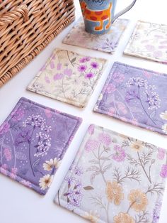 four coasters with flowers on them sitting next to a basket and coffee cup in it