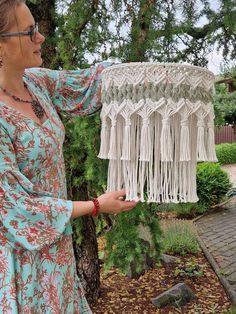 a woman is holding up a piece of crocheted material in front of a tree