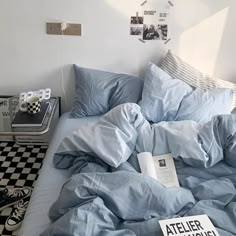 an unmade bed with blue sheets, pillows and pictures on the wall above it