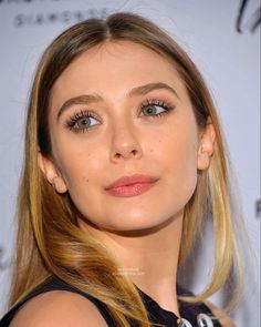 a close up of a person with long blonde hair and green eyeshadow, wearing a black dress