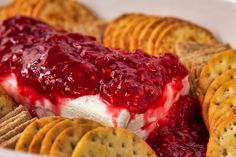 a bowl filled with crackers and cheese covered in cranberry sauce next to crackers