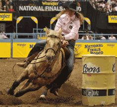 a woman riding on the back of a brown horse next to a barrel in front of a crowd