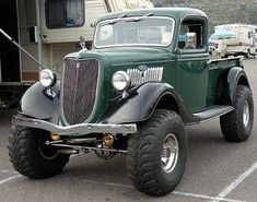 an old green truck parked in a parking lot next to a camper and trailer