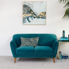 a blue couch sitting next to a table with a plant on it and a painting above it