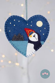 a heart shaped ornament hanging from a string with a penguin on it's head