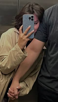 a woman holding her phone up to her face while standing next to a man in an elevator