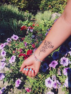 a woman's arm with a flower tattoo on it and flowers in the background