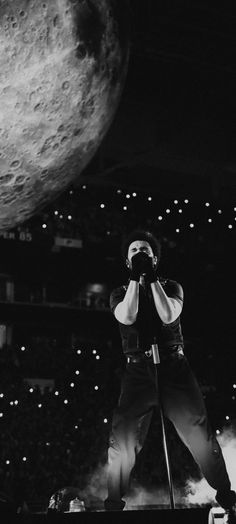 a man standing on top of a stage next to a giant moon in the background