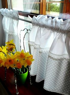 yellow daffodils in a green vase on a window sill next to white curtains